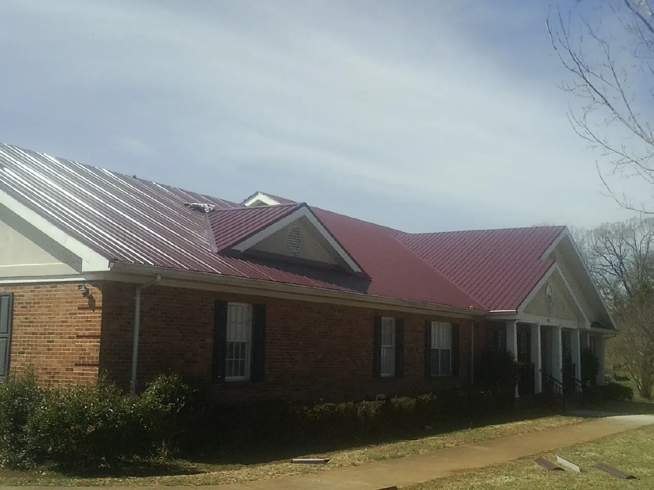 Red metal roof with gabled entries on a long brick building, from a Hail Damage Roof Repair job in Dundalk