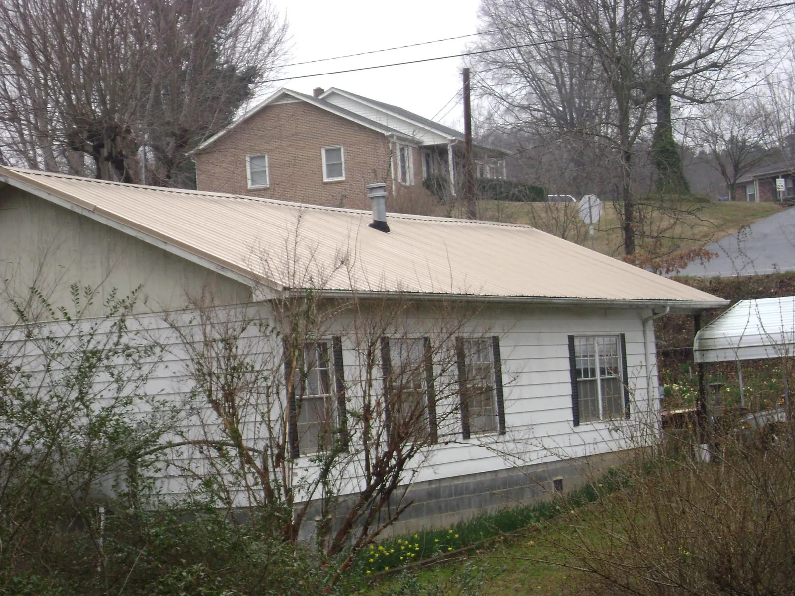 Tan metal roof on a white sided house set into a hillside — Commercial Roofing by Roofing Brothers in Dundalk